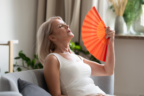 Starejši ženski, v menopavzi, je vroče. Hladi se s pahljačo.