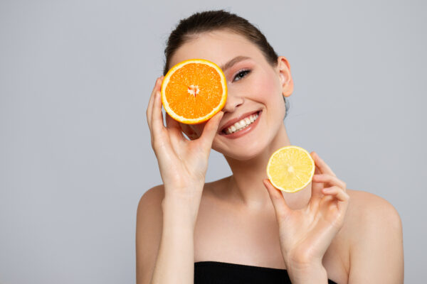 lepa mlada ženska kaže rezini pomaranče in limone za beljenje zob